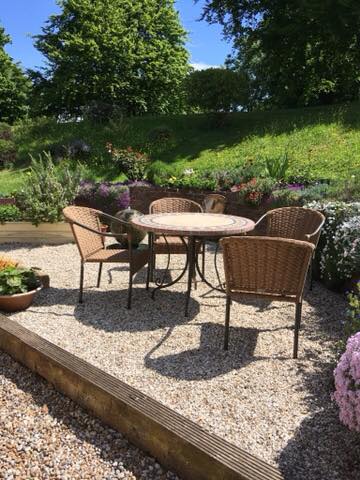 Garden table and four chairs in front of grass bank and a tree