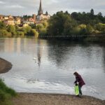 Women walking beside the river with church spire in background