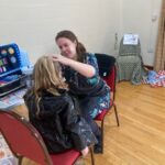 Child having her face painted by a woman