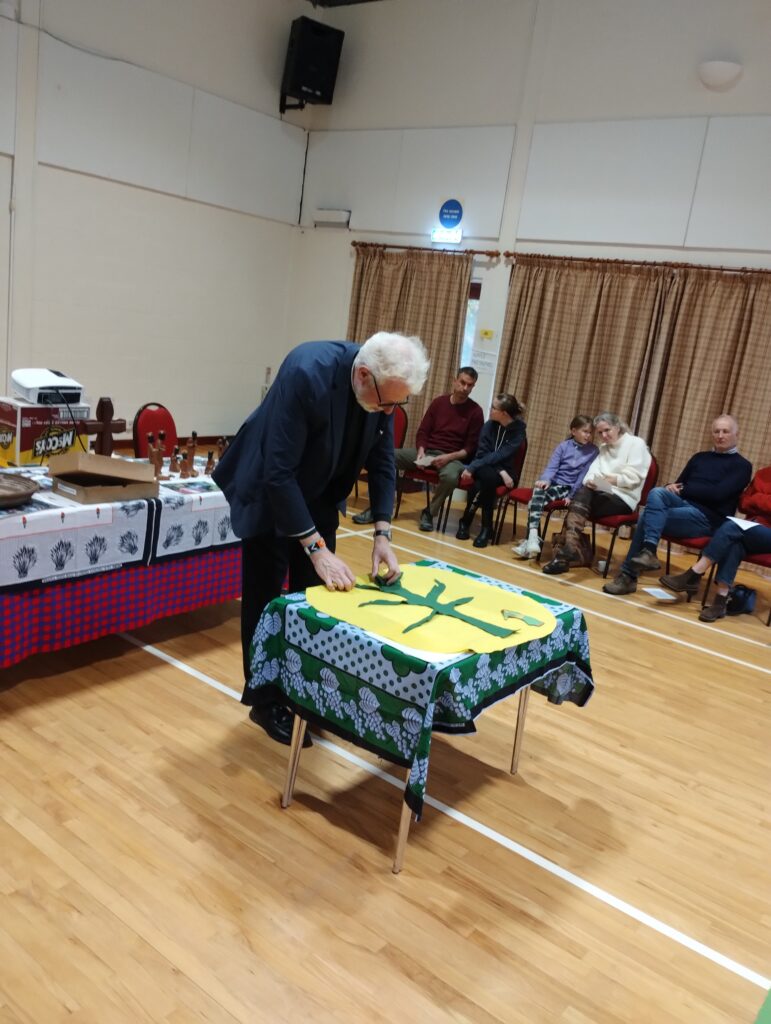 vicar bending over a table watched by people sitting down