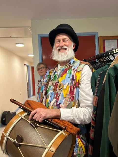 A male morris dancer wearing multicoloured clothes and holding a drum