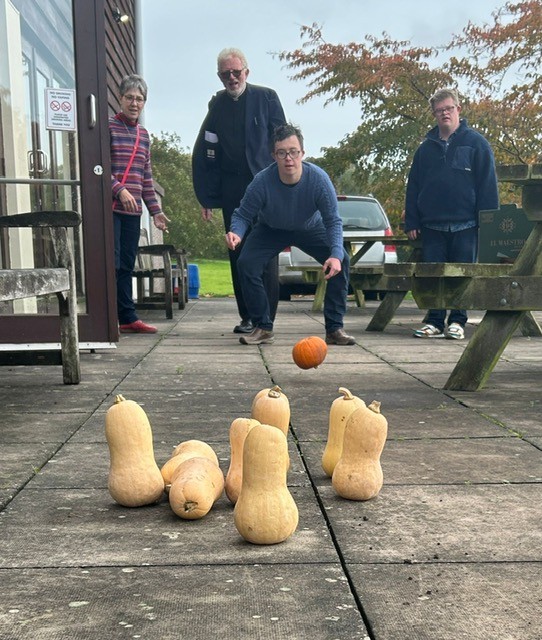 Three people watching a man bowling a pumpkin at squash skittlers