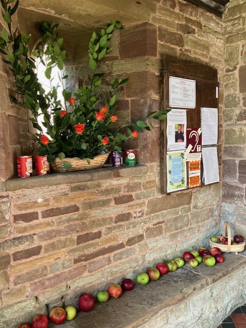 Orange roses, apples and tins of food in the church porch