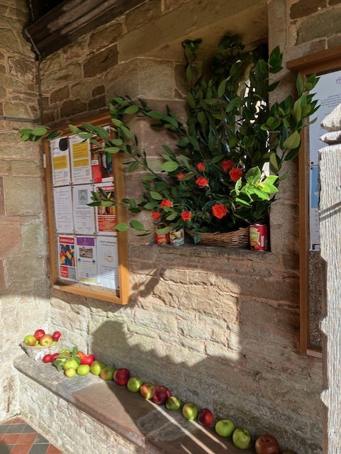 Orange roses, apples and tins of food in the church porch