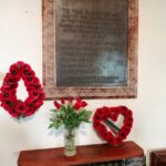 war memorial in the church with two red poppy wreaths and red flowers