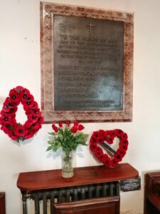 war memorial in the church with two red poppy wreaths and red flowers